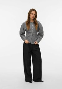 Šedý pletený kardigan se zapínáním na knoflíky, balónovými rukávy a volným střihem, doplněný širokými černými kalhotami a černými špičatými botami.