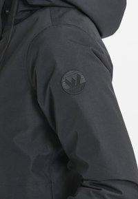 Czarny rękaw kurtki z okrągłą naszywką z logo Whistler Denmark na górnej części ramienia, ukazujący fakturę tkaniny i szew.