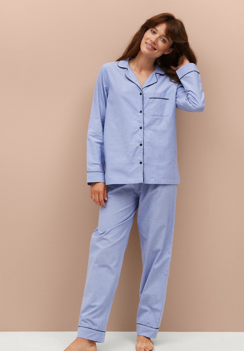 Lichtblauw pyjamastel in zachte stof, met een knoopsluiting shirt met een zak en contrasterende zwarte bies, gecombineerd met bijpassende broek.