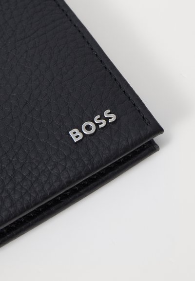 Portefeuille en cuir noir avec une surface texturée et des coutures visibles. Présente un accent en argent avec le logo "BOSS" sur le devant.