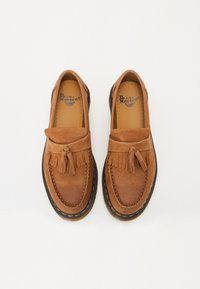 Hnědé velurové mokasíny s třásněmi, s šitím ve stylu mokasín a černou gumovou podrážkou se žlutými akcenty. Vnitřní branding Dr. Martens.
