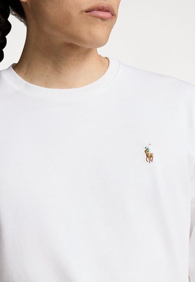 Hvid bomuldscrewneck sweater med et lille broderet polo spiller logo på venstre bryst. Glat tekstur, afslappet pasform.