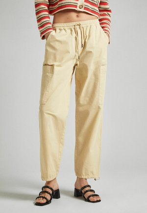 Pantaloni cargo beige con vita elastica e cordoncino, dotati di tasche laterali e polsini arricciati. Tessuto texturizzato, vestibilità rilassata.
