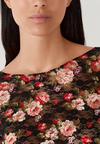 Kantenshirt met een bloemenpatroon in rood en roze op een zwarte achtergrond. De halslijn is breed en zachtjes gebogen.