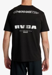 Čierne bavlnené tričko s grafikou textu na zadnej strane v bielej a šedej farbe, s rôznymi písmami a vzormi, vrátane "RVCA" a ďalších detailov.