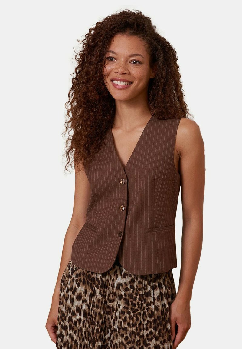 Gilet marron sans manches avec un motif à fines rayures, doté d'un col en V, de cinq boutons et de deux poches avant, porté sur une jupe imprimée léopard.