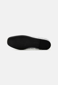Scarpa bianca slip-on con una texture superiore a quadretti, suola in gomma con grip a motivo e dettagli neri sul fondo.