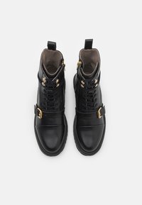 Sorte lær ankle boots med gullhardware, snøring og glidelås på siden. Inkluderer en kontrasterende matt tåhette og justerbar spenne.