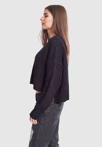Pull en tricot noir court avec un motif texturé, des manches longues et un col arrondi, associé à un jean noir déchiré.