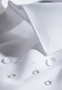 Camisa de tela blanca con cuello doblado, que presenta múltiples gotas de agua en la superficie, destacando su textura resistente al agua.