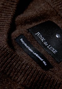Brauner Strickpullover mit gerippter Textur, ausgestattet mit einem schwarzen Etikett, auf dem "JUNK de LUXE" und "Recycled Italian Lambswool Mix" steht.