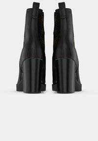 Bottes noires à la cheville avec une finition brillante, équipées d'un talon épais et d'accents en motif élaboré sur les côtés. Texture lisse et design épuré.
