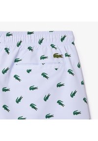 Costume da bagno azzurro chiaro con un motivo di coccodrilli verdi e una tasca sul retro. La cintura è elastica, per una vestibilità comoda.