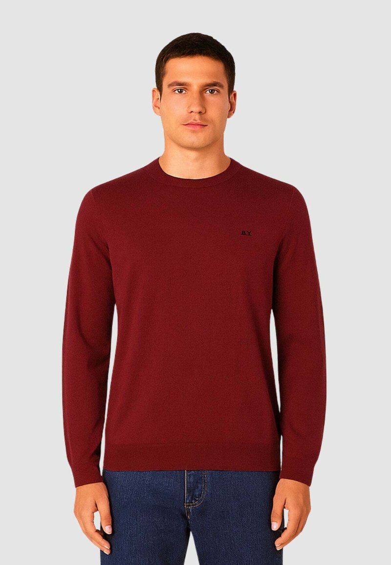 Maglione bordeaux con maniche lunghe, scollatura rotonda e polsini a costine. Presenta un piccolo logo nero sul lato sinistro del petto. Il tessuto sembra liscio.