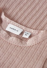 Heller rosa Rippstrickstoff mit einem gewellten Spitzenkragen. Etiketten zeigen die Marke "name it" und die Größe 2-4 Monate. Dezentes Muster im gesamten Stoff.