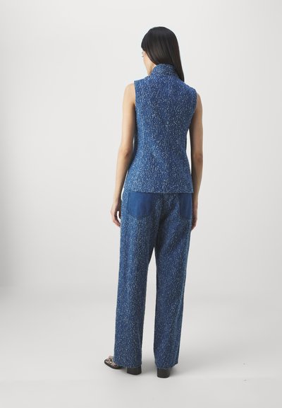 Blue textured sleeveless top with a high collar, paired with loose-fit blue pants featuring two back pockets. Smooth fabric with a subtle shine.