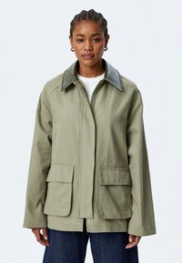 Olivgrön jacka med stora framfickor, svart krage och avslappnad passform. Tillverkad av textil, med dragkedjestängning.