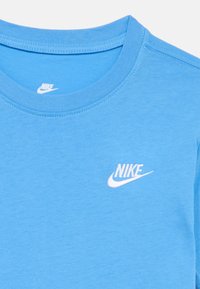 Ανοιχτό μπλε μπλουζάκι Nike με λευκό λογότυπο Nike στο στήθος και εσωτερική ετικέτα στη γραμμή του λαιμού.