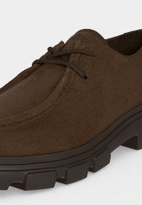 Chaussure à lacets en daim marron avec une épaisse semelle en caoutchouc foncé et un motif de semelle robuste, gros plan montrant la partie latérale et avant supérieure.