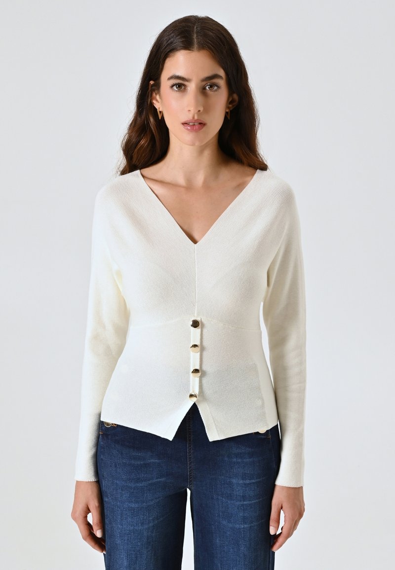 Maglione lavorato a maglia avorio con scollo a V, maniche lunghe e cinque bottoni oro sulla parte anteriore. Vestibilità su misura con orlo curvo.