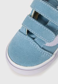 Blauer Wildledersneaker mit doppelten Klettverschlüssen und weißer Gummisohle auf weißem Hintergrund.