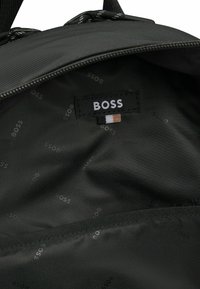 Czarny materiał wewnętrzny plecaka z metką logo "BOSS". Wzór z powtarzającym się tekstem "BOSS", zawiera kieszeń wzdłuż szwu.