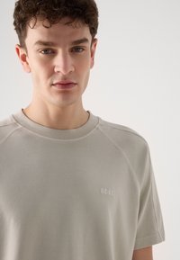 Světle šedý crewneck sweatshirt s krátkými rukávy, na hrudi s jemně vyšitým logem "BOSS" a hladkou, jemnou strukturou.