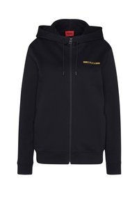 Felpa nera con zip realizzata in tessuto morbido, dotata di cappuccio con coulisse, tasche frontali e logo dorato sul petto. Vestibilità regolare.