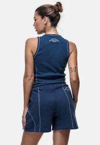 Set di top sportivo e pantaloni corti di colore blu navy realizzato in tessuto elasticizzato, con cuciture bianche e un logo ricamato sul retro.