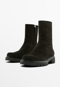 Stivali ankle in suede nero con una silhouette dritta, suola in gomma robusta e dettaglio con zip laterale. Texture liscia con una finitura opaca.