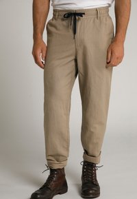 Pantalons décontractés beiges avec taille élastique et cordon de serrage bleu marine, présentant une coupe droite et des ourlets retroussés, assortis à des bottes brunes à lacets.