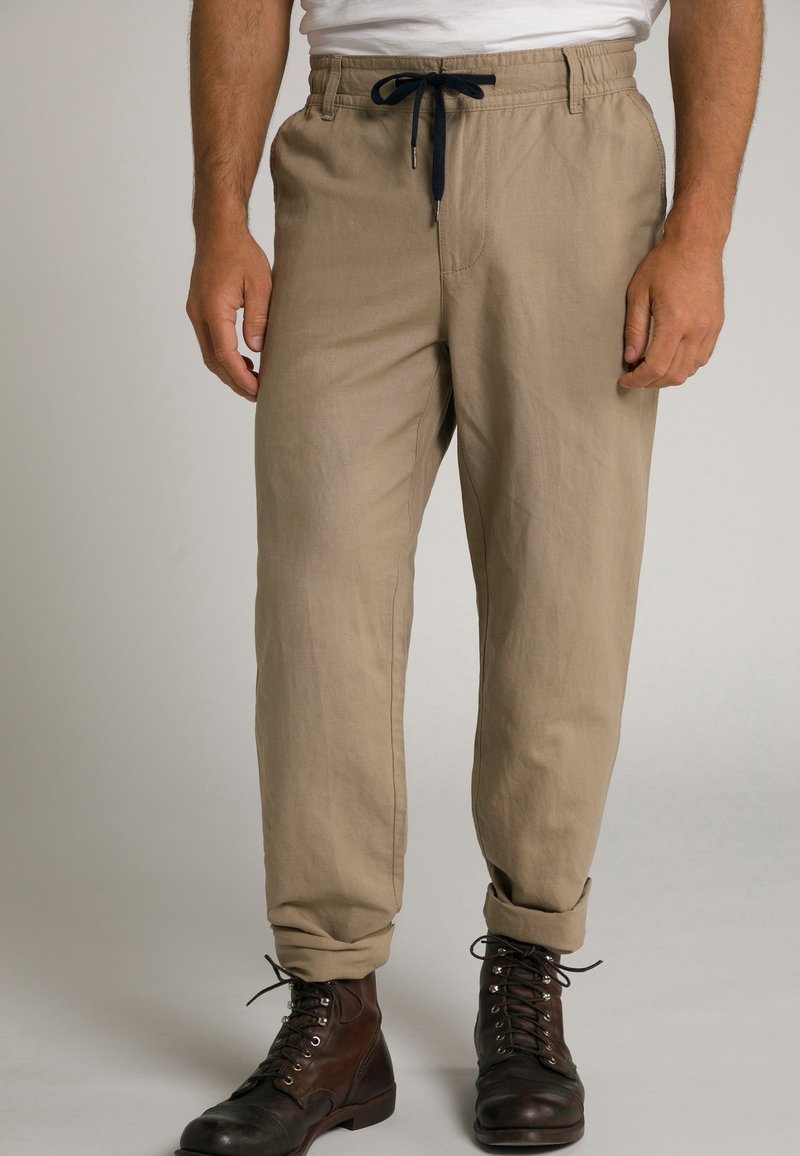Pantalons décontractés beiges avec taille élastique et cordon de serrage bleu marine, présentant une coupe droite et des ourlets retroussés, assortis à des bottes brunes à lacets.