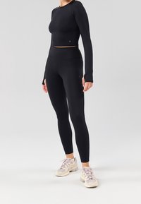 Czarny długi rękaw crop top w połączeniu z czarnymi legginsami o wysokim stanie; gładka tekstura; uzupełnione jasnymi butami sportowymi.