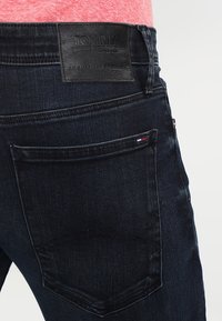 Tmavě modré denimové džíny s koženou nášivkou Tommy Jeans na zadní straně. Mají jedno zadní kapsu s malým detailním logem.