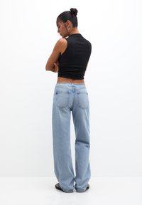 Schwarzes, kurz geschnittenes Bustier kombiniert mit hellblauen, weit geschnittenen Jeans, die ein klassisches Fünf-Taschen-Design und dezente Nähte auf der Rückseite aufweisen.