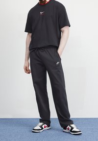 Černé tričko Nike s červeným akcentem a logem, spárované s černými tepláky se stahovací gumou, bílým logem Nike a černo-bílými teniskami.