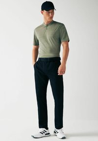 Grønstribet polo skjorte med krave, sorte bukser, sorte kasket og hvide sneakers med sorte accenter. Fokus på simpel, funktionel design.