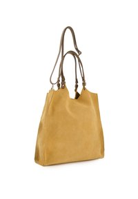 Sac fourre-tout en suédine douce couleur beige clair, avec deux poignées courtes et une bandoulière longue réglable, se tenant debout sur un fond blanc.