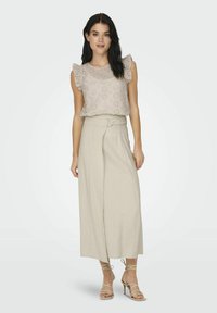 Beige bestickte Bluse mit Rüschensäumen, kombiniert mit einem hoch taillierten, hellbeigen weiten Rock und beigen Sandalen mit Riemchen.