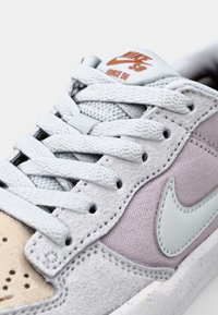 Sneaker grigio e lavanda con pannelli in suede testurizzato e mesh. Presenta il logo Nike bianco, lacci grigi e una punta beige.