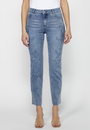 Lyseblå skinny jeans med broderede blomster mønstre på forbenene, båret med klare hælede sandaler og en hvid top.
