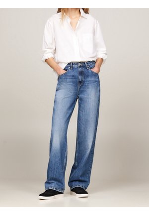 Light blue wide-leg jeans made of denim, featuring a high waist, two front pockets, and minimal stitching details, paired with black sneakers.