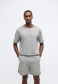 Σετ γκρι βαμβακερό μπλουζάκι με κοντά μανίκια και σόρτς, με στρογγυλή λαιμόκοψη και αντίθετες ραφές. Λογότυπο σε κόκκινο στο στήθος. Χαλαρή εφαρμογή.