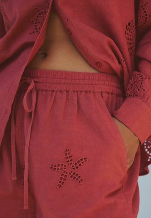 Rotes Leinen-Loungewear-Set mit einem Hemd zum Knöpfen mit Ösen-Details und passenden Shorts mit Seestern-Ausschnittmuster an der Tasche.