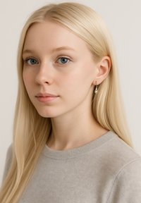 Guldörhängen med droppdesign, bärs av en person med långt, rakt blont hår, mot en neutral bakgrund.