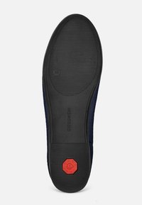 Semelle en caoutchouc noir avec une surface texturée, arborant un accent octogonal rouge avec un logo, entouré d'un dessus en textile bleu marine.