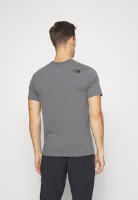 Šedé tričko s krátkým rukávem kulatým výstřihem a černým logem značky The North Face na horní části zad, vyrobené z měkké, texturované látky.