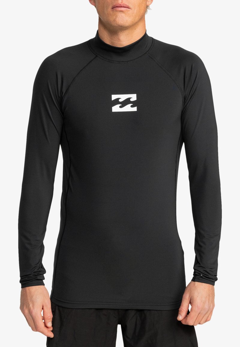 Rash guard de manga larga negra, hecho de material elástico, con un collar alto y un logo de ola blanca en el pecho.
