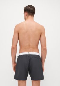 Bañador gris hecho de un tejido ligero, con una cinturilla elástica blanca, un bolsillo trasero y un sutil brillo.