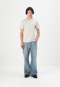 T-shirt en coton gris clair avec un col rond, associé à un jean en denim bleu clair évasé. Le modèle porte des chaussures noires. Design simple et minimaliste.